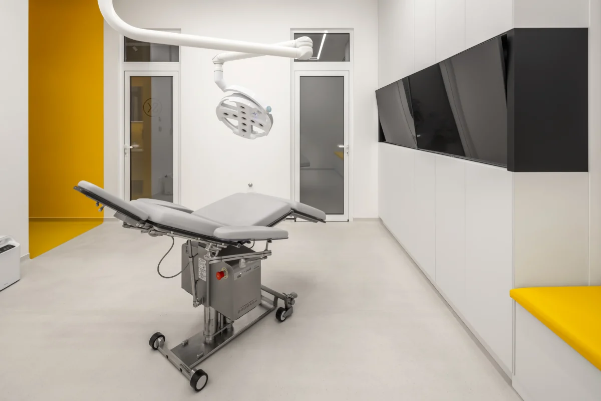Modern examination room with an adjustable table, overhead lighting, built-in cabinets and yellow accents – dental clinic design by SPACE DESIGN
