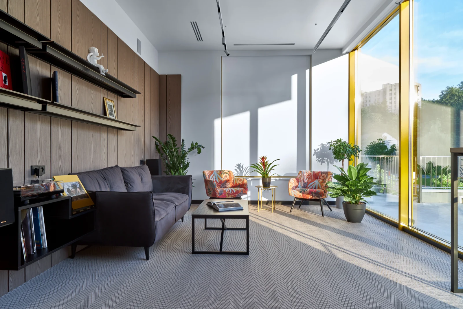 Poczekalnia przy panoramicznych oknach: szara sofa, kolorowe fotele, rośliny i drewniane półki
